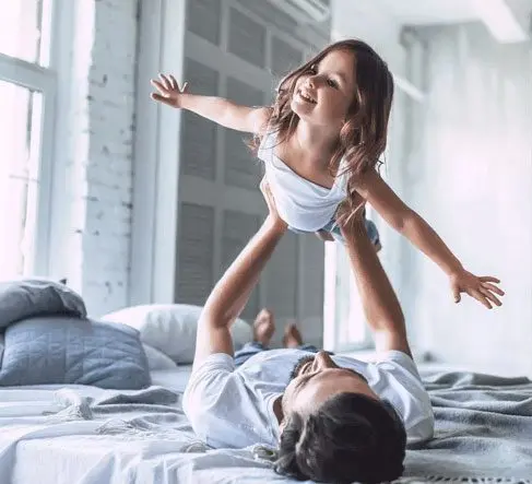 A man and his daughter playing on the bed